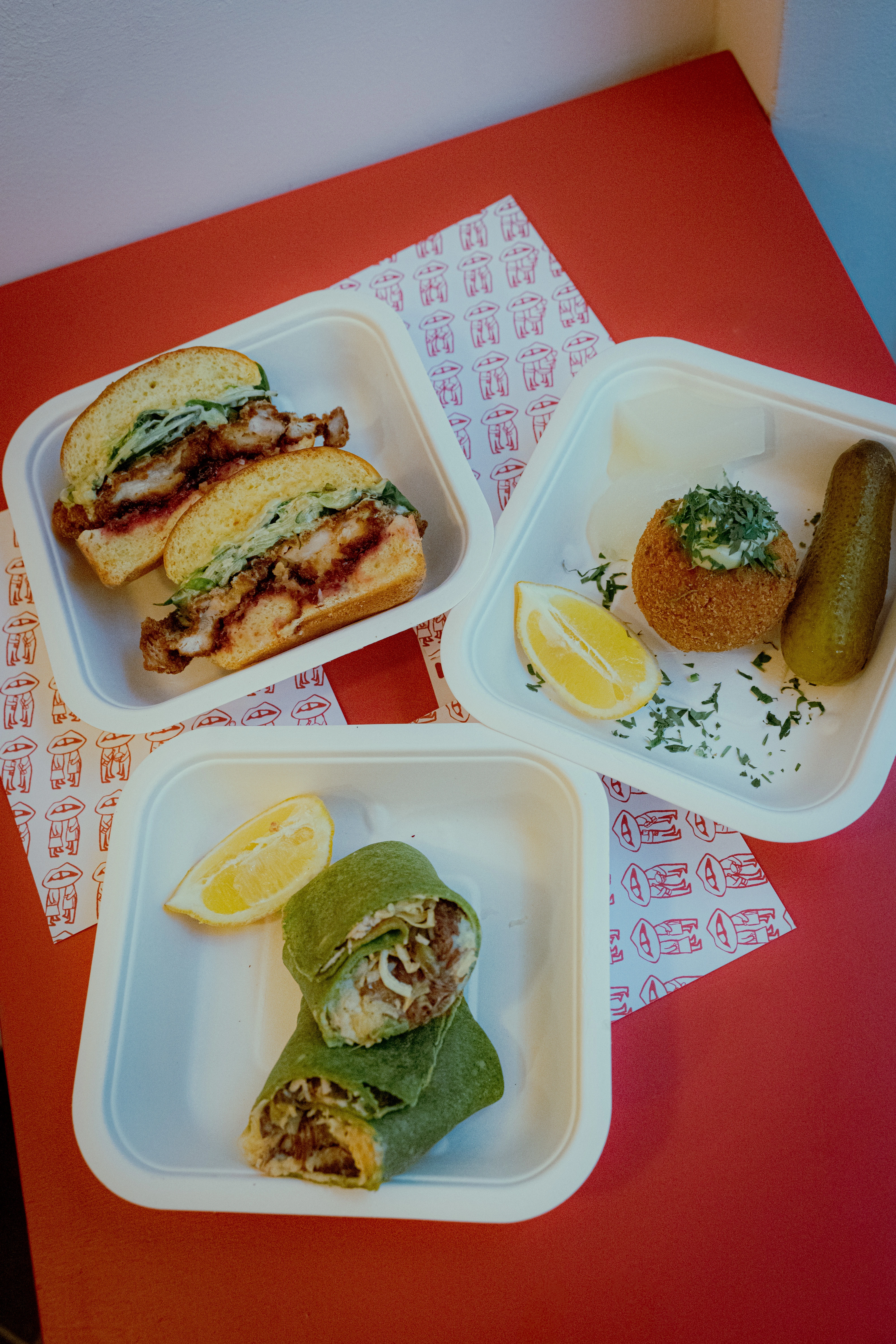 Leckeres Essen: Sandwich, Wrap, Scotch Egg und Gurken auf rotem Hintergrund.